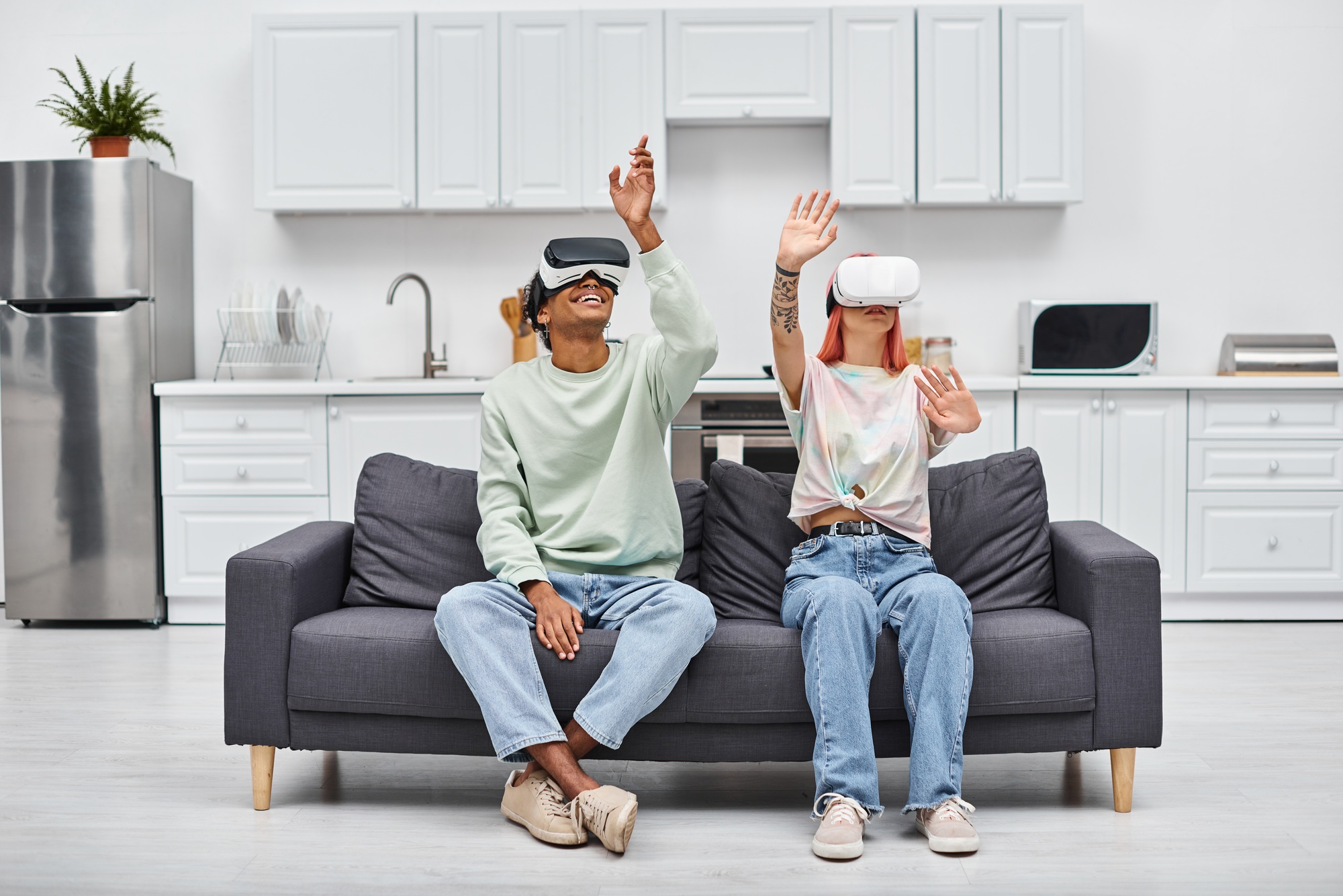 good looking jolly interracial couple sitting on sofa in living room at home with VR headsets